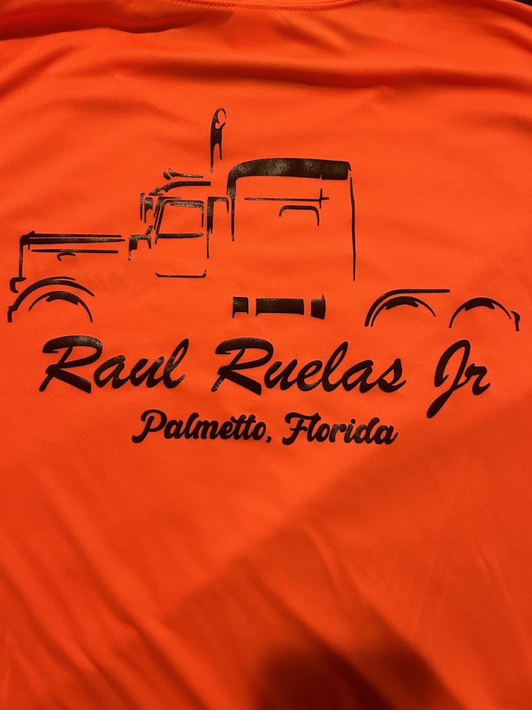 Bright orange dri-fit shirt with a black screen-printed truck design